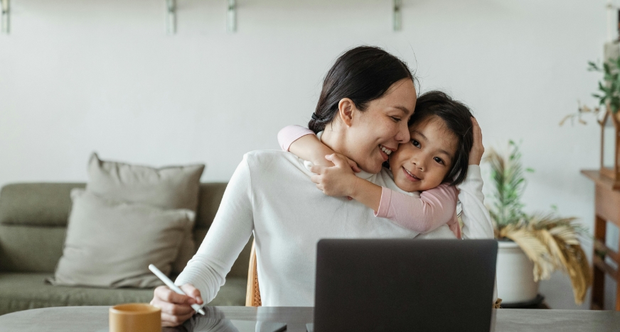 a kid hugging her mom while she's working.