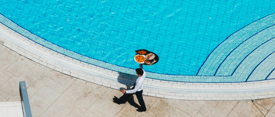 a man carrying a tray of food by a pool.
