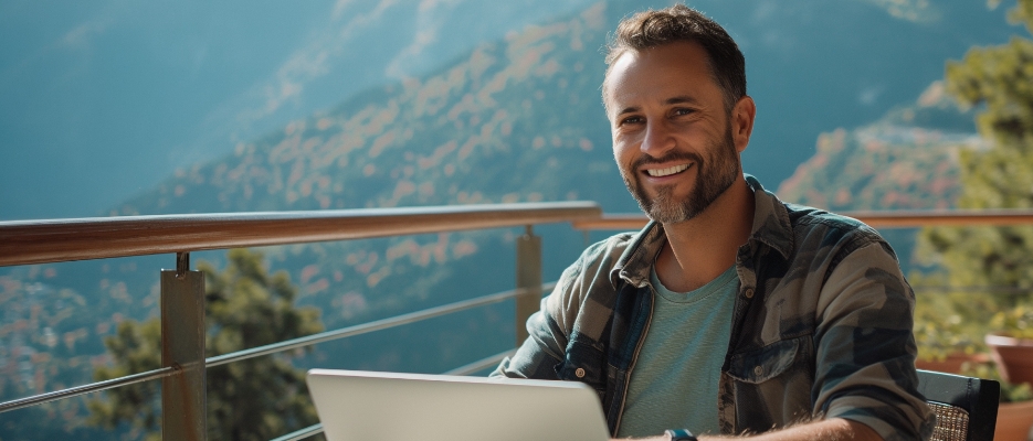 a man smiling while using a laptop outside.