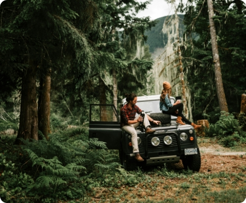 a couple sitting on their car while in the woods.