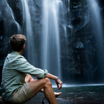 a man sitting and looking at a waterfall.