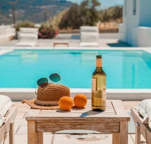 a hat, sunglasses, oranges, and wine on a poolside table.