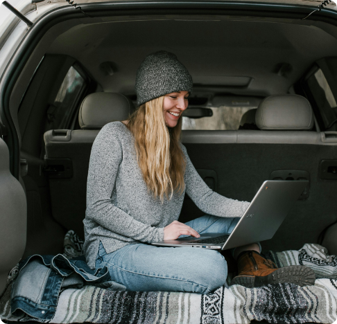 a woman in the trunk of her car on a laptop.