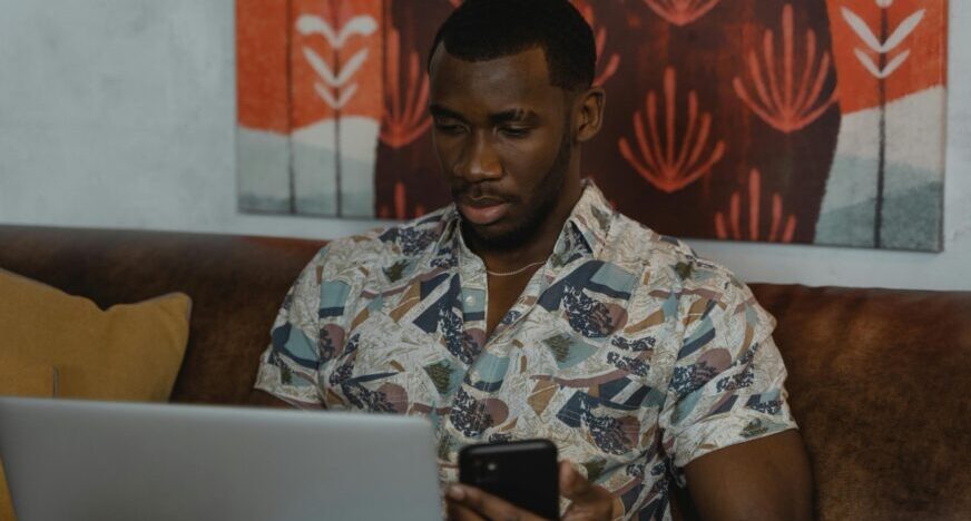 a man using his phone and a laptop.