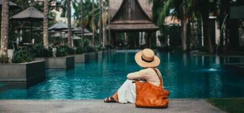a woman sitting at a pool with an orange bag.