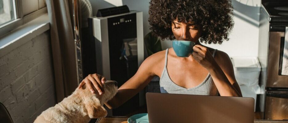 a woman sipping from a mug and petting a dog